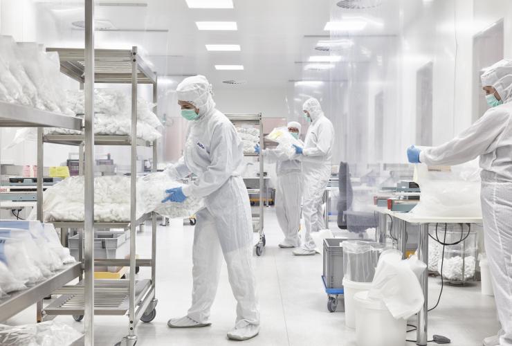 ALPLApharma workers in protective suits organize and inspect plastic packaging in a clean, bright facility.
