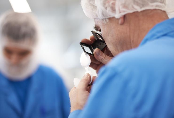Technician inspects plastic packaging sample with magnifier in a clean production setting.