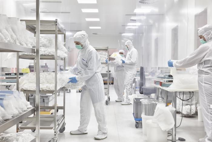 ALPLApharma workers in protective suits organize and inspect plastic packaging in a clean, bright facility.