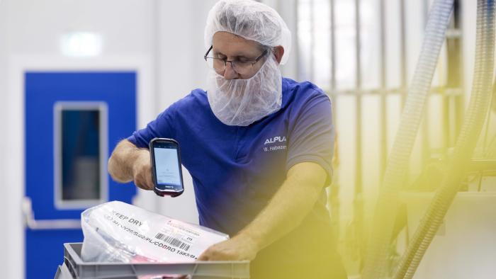 Worker in ALPLA uniform scans packaging in a clean, modern production facility.
