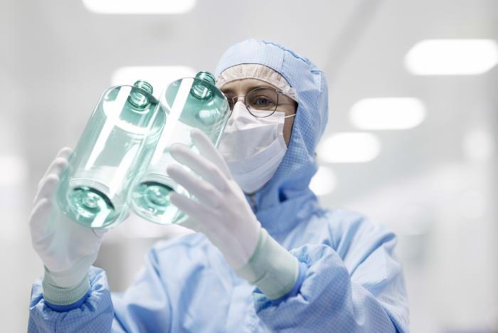 Technician inspects clear plastic bottles in a sterile, high-tech production facility.